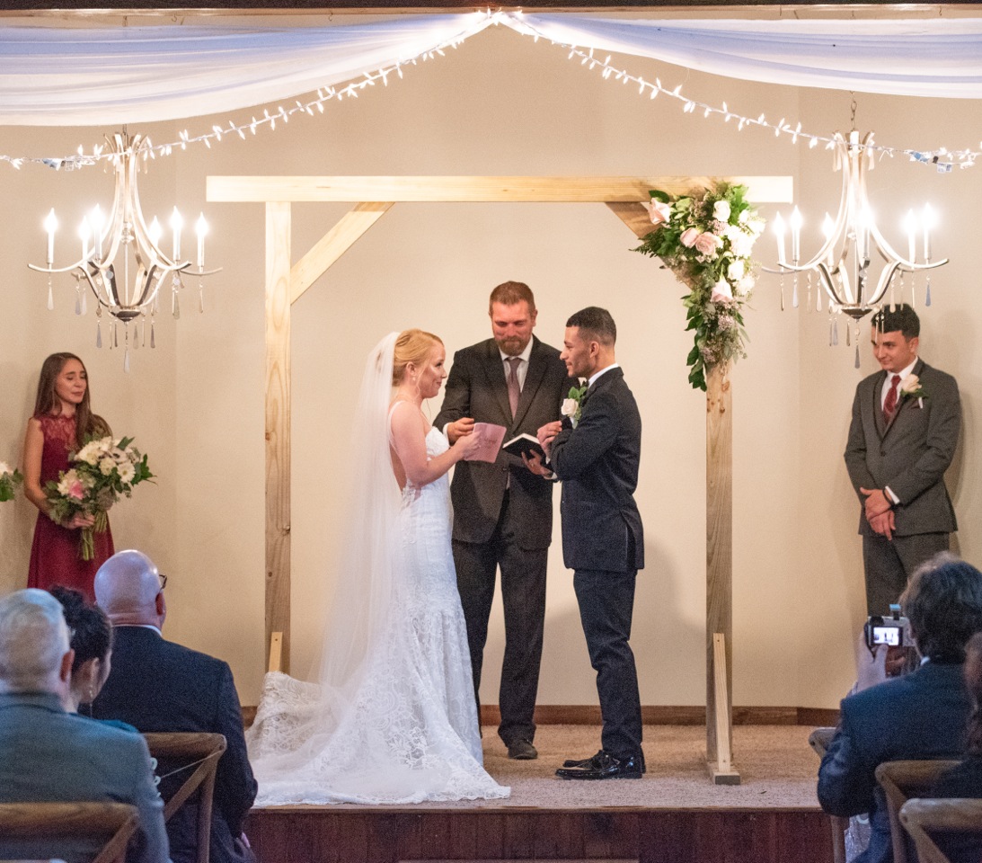 An indoor ceremony on the stage with a movable cedar wood arbor and chandeliers