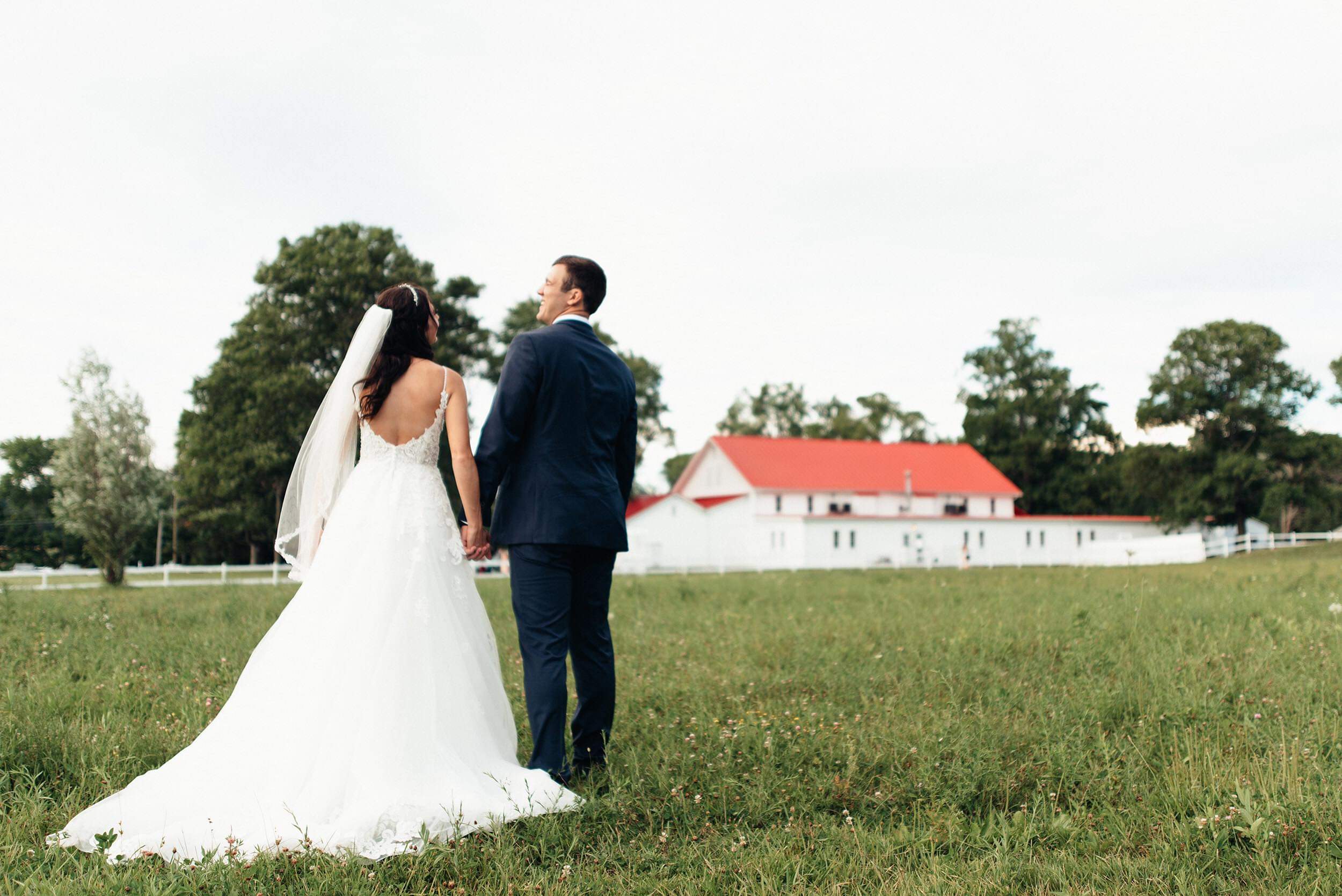 Bride and groom hold hands in the meadow overlooking Columbia Ballroom